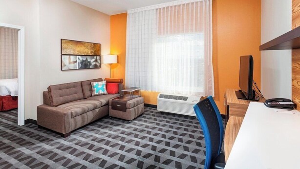 Une chambre d’hôtel avec un canapé, une petite table, une télévision et une fenêtre avec des rideaux.
