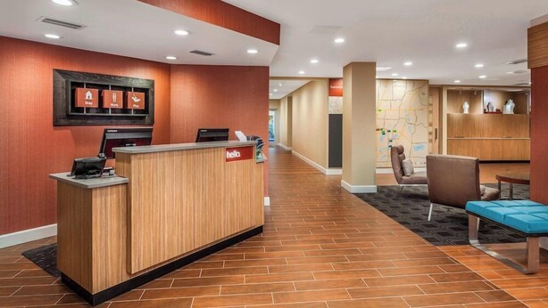 A hotel reception area with a wooden reception desk, a seating area with a blue bench, and a map on the wall. - Towneplace Suites by Marriott Orlando Altamonte Springs/maitland (Altamonte Springs)