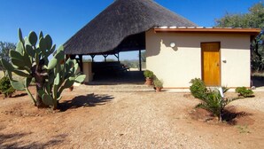 A single-story building with a thatched roof, a wooden door, and a gravel driveway. - Etango Ranch Guest Farm (Windhoek)