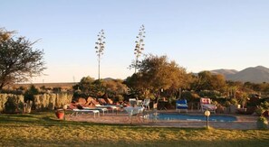 A pool area with lounge chairs, a pool, and a mountainous backdrop. - Etango Ranch Guest Farm (Windhoek)
