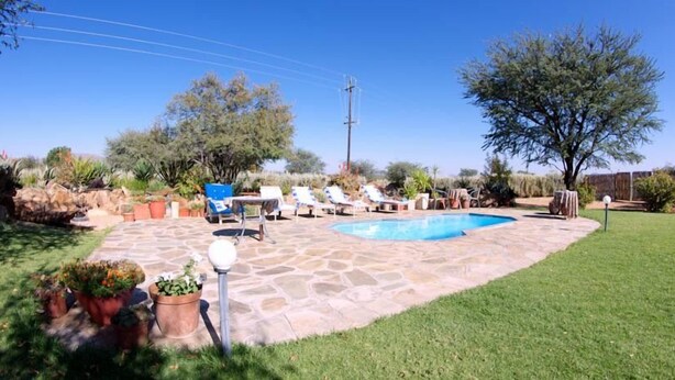 A backyard with a swimming pool, stone patio, and outdoor furniture. - Etango Ranch Guest Farm (Windhoek)