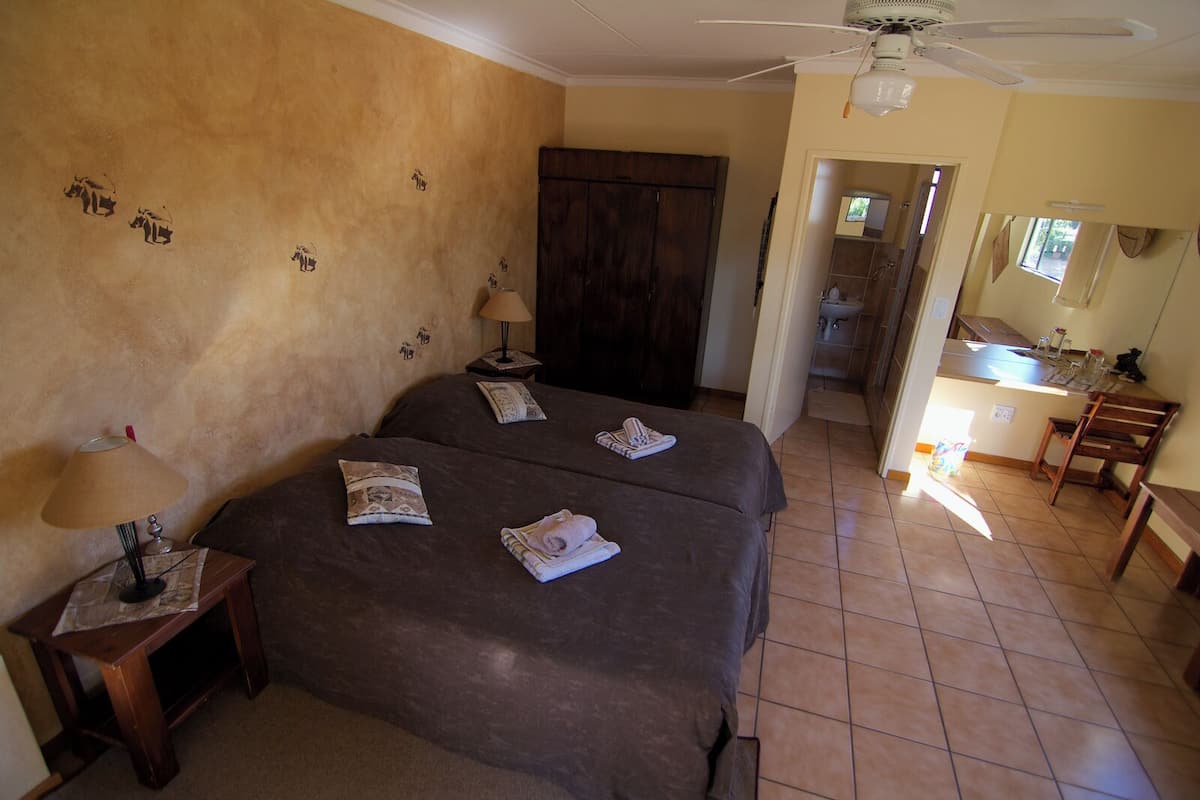 A hotel room with two beds, a wooden wardrobe, a bathroom visible through an open door, and a small kitchenette area.