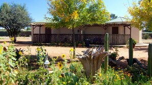 A house with a wooden fence, a tree with yellow leaves, and various plants in the garden. - Etango Ranch Guest Farm (Windhoek)