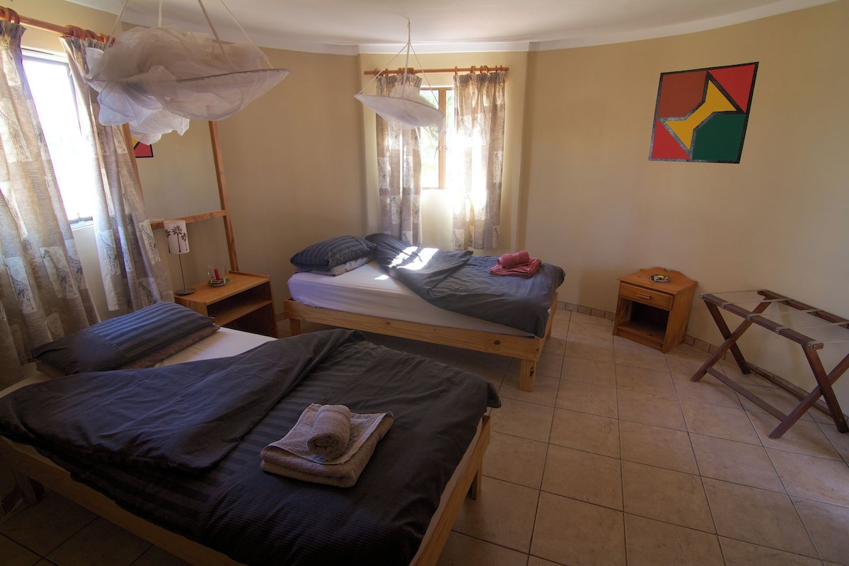 A bedroom with two beds, a wooden floor, a small table, and a wall art piece.