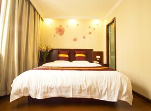 Een hotelkamer met een groot bed, een houten hoofdeinde en een vaas met bloemen op het nachtkastje.