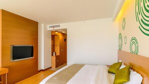 A modern hotel room with a large bed, a TV mounted on the wall, and a wooden wardrobe.