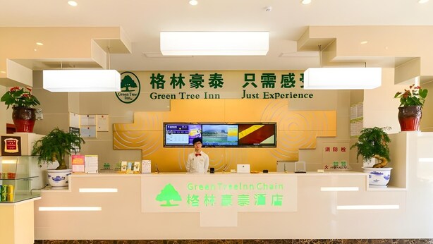 A hotel reception area with a modern design, featuring a reception desk, digital display screens, and potted plants.
