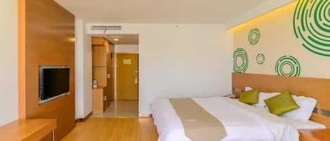 A hotel room with a bed, a TV, a wooden bench, and a wall with circular patterns.