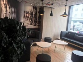 Un interior moderno con un sofá, dos mesas blancas y una planta verde grande.