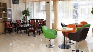 A hotel lobby with a reception desk, a seating area with wooden and modern chairs, a small round table, and large windows with curtains.