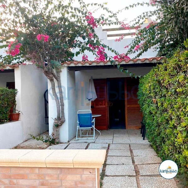 A courtyard with a tiled roof, a wooden bench, a blue chair, and a potted plant. - Kartibubbo Beach Resort (Campobello di Mazara)