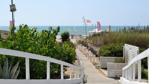 A pathway leading to a beach with a white railing, flags, and a clear view of the ocean. - Kartibubbo Beach Resort (Campobello di Mazara)