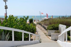 A pathway leading to a beach with a white railing, flags, and a clear view of the ocean. - Kartibubbo Beach Resort (Campobello di Mazara)