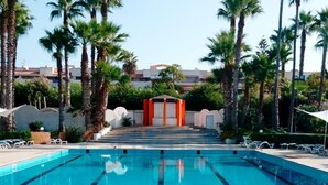 A swimming pool with clear blue water, surrounded by palm trees and a building in the background. - Kartibubbo Beach Resort (Campobello di Mazara)