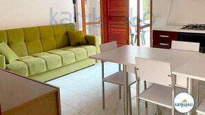 Una sala moderna con un sofá verde, una mesa de comedor con sillas y una cocina con armarios y estufa.