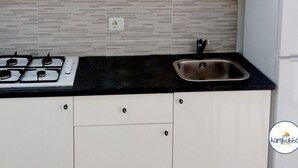 Una cocina con armarios blancos, encimera negra, pileta de acero inoxidable y estufa a gas.