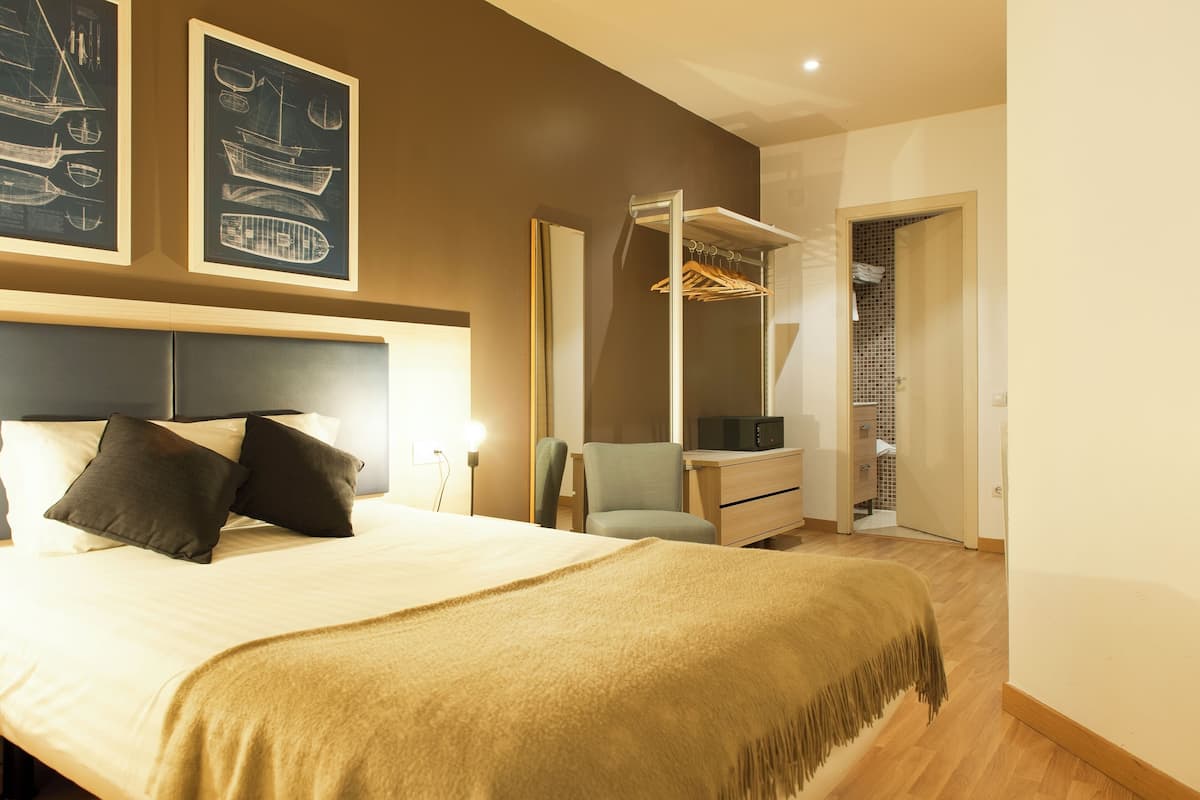 A modern bedroom with a large bed, a bedside table, a chair, a wardrobe, and a mirror.