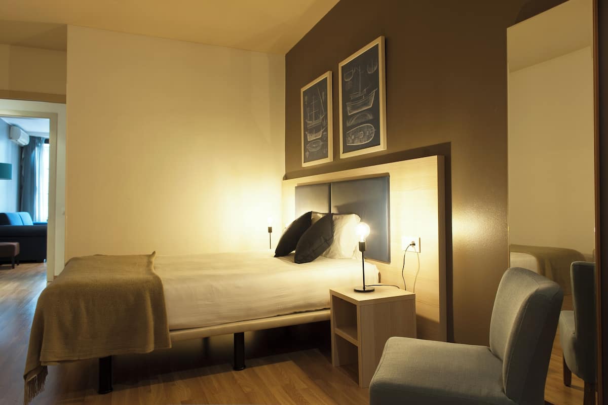 A hotel room with a bed, bedside tables, a chair, and artwork on the wall.