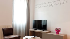 A modern living room with a leather chair, a round table with books and a remote, a flat-screen TV on a wooden stand, and a decorative wall with a quote. - MH Apartments Ramblas (Barcelona)