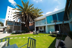 A modern building with a large palm tree, a patio with outdoor furniture, and a clear sky. - Camino Plaza (Cochabamba)