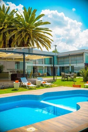 Une piscine avec des chaises longues, un patio couvert et des palmiers.