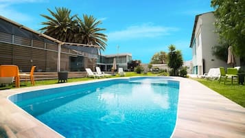 A swimming pool with lounge chairs, a modern building, and a palm tree.