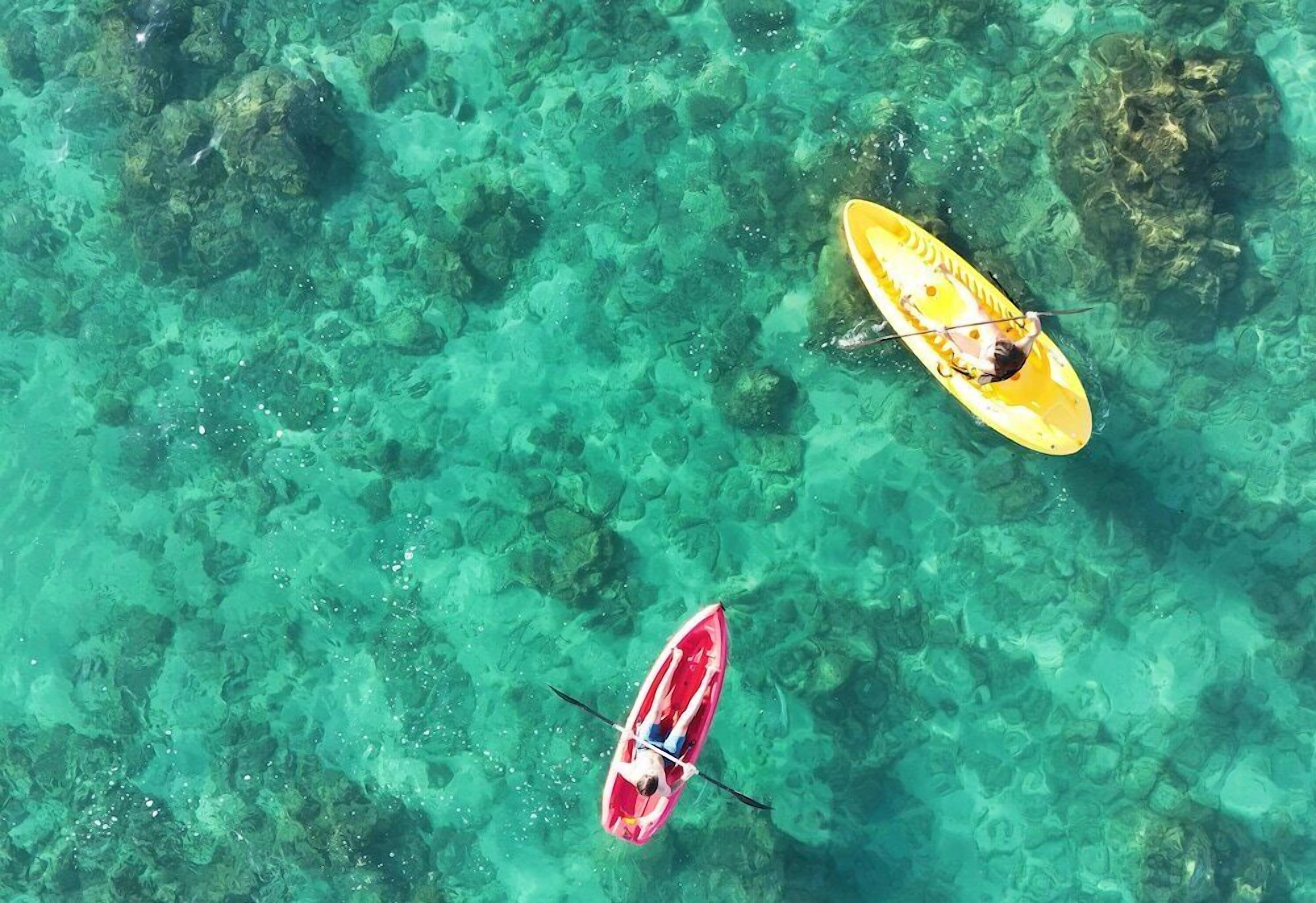 Two kayaks on a clear, shallow body of water with visible underwater rocks.