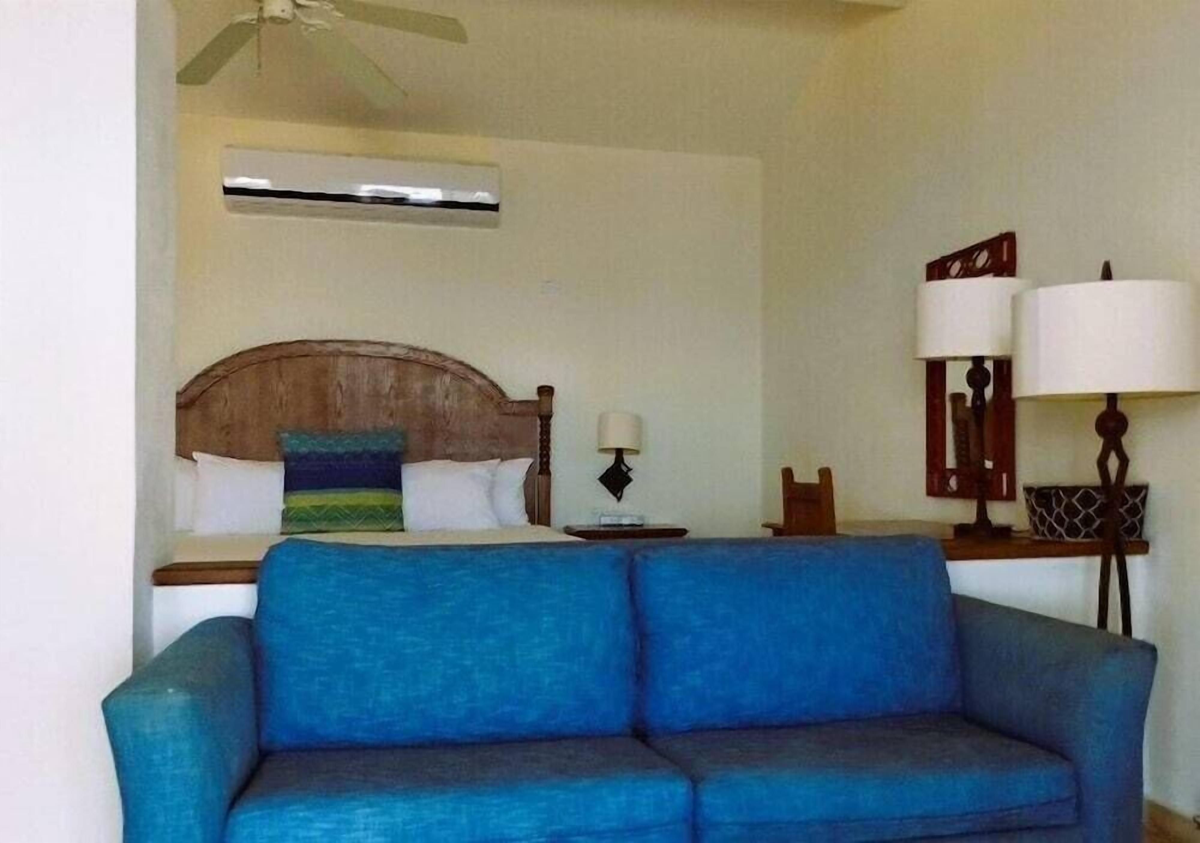 A room with a bed, a blue sofa, a nightstand with a lamp, and a ceiling fan.