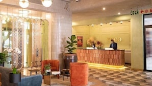 A hotel reception area with a wooden reception desk, a receptionist, and a seating area with a round wooden table and chairs. - Hyde Johannesburg Rosebank (Johannesburg)