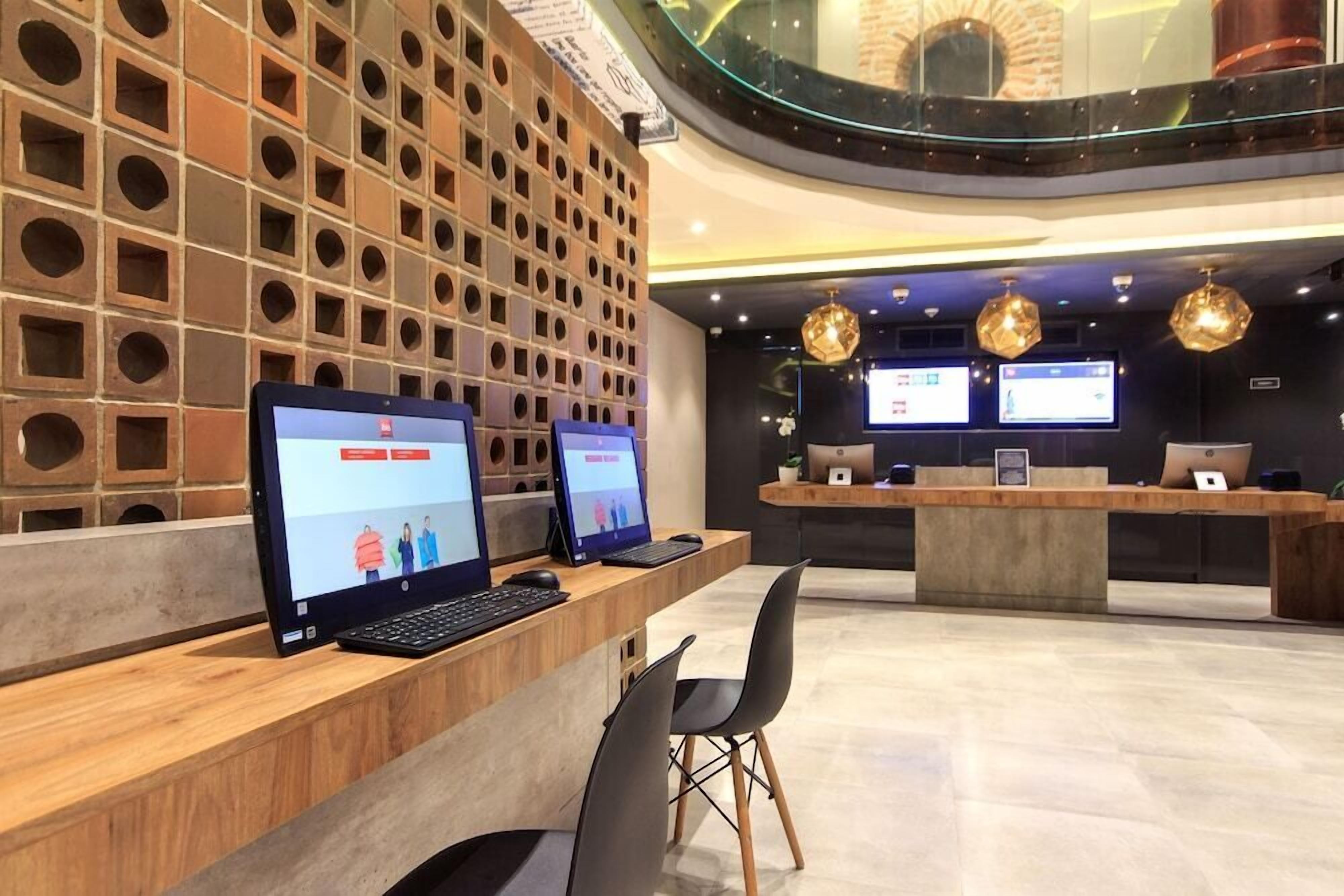 Un área de recepción moderna con pared de ladrillo, varias estaciones de trabajo con computadoras y un mostrador central.