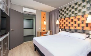 Habitación de hotel con cama, escritorio, televisión, aire acondicionado y una pared con diseño geométrico.
