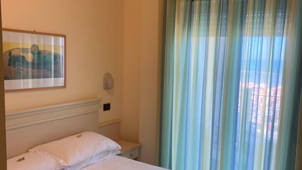 Habitació d'hotel amb un llit gran, una vetusta, una làmpada penjada a la paret i una finestra amb cortines a ratlles.