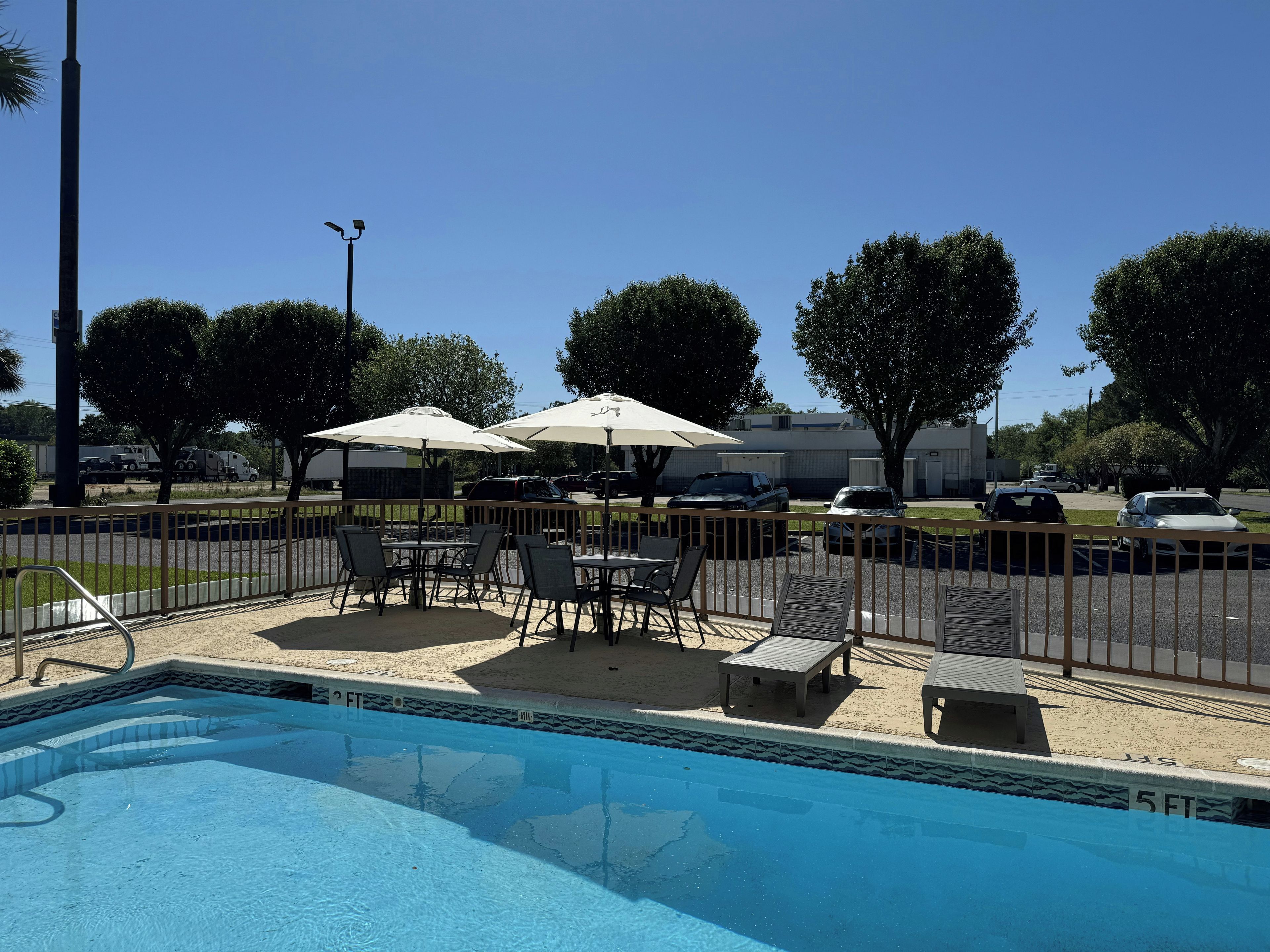 A swimming pool with a fenced patio area, outdoor seating, and umbrellas.