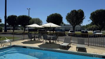 A swimming pool with a fenced patio area, outdoor seating, and umbrellas.
