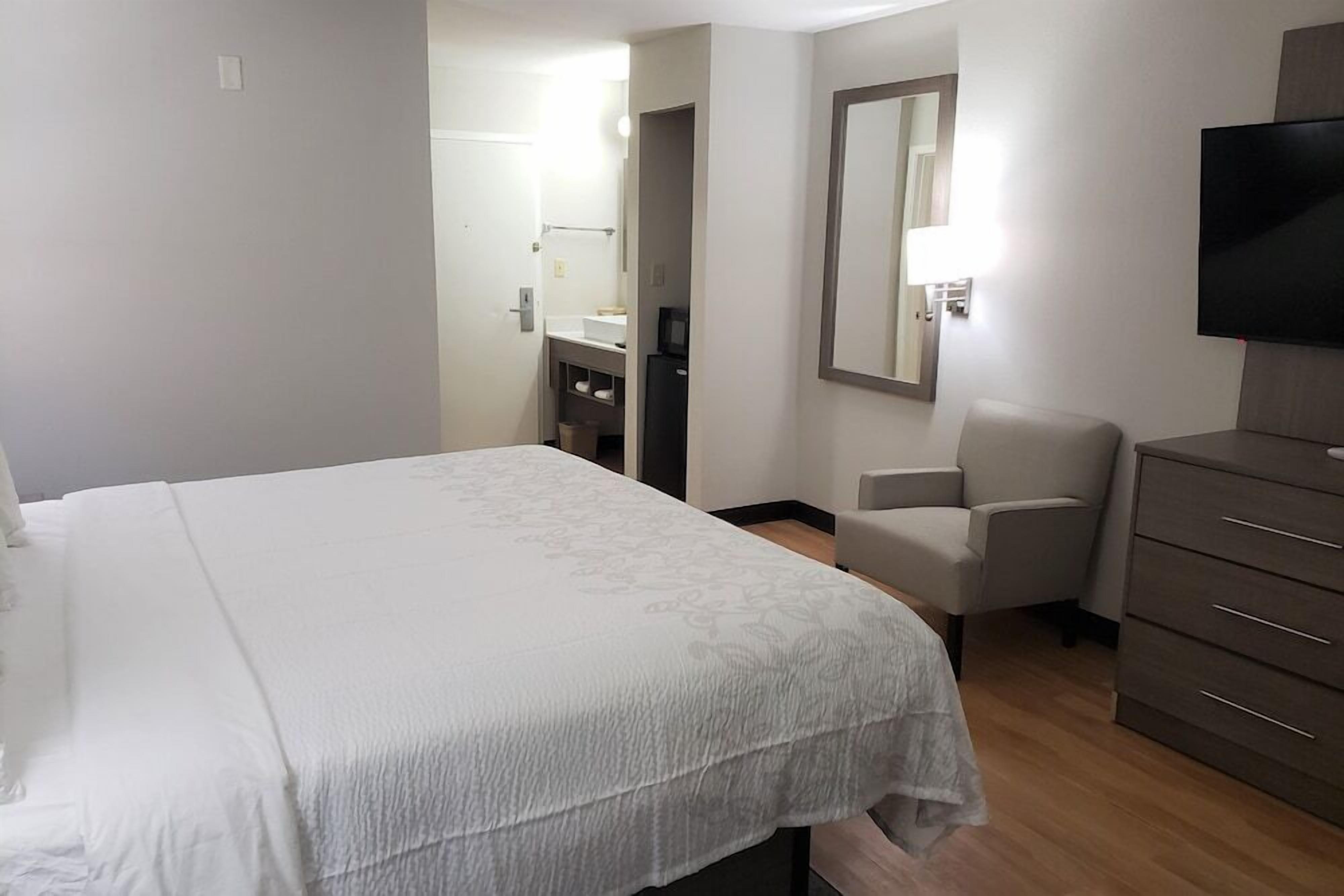 A hotel room with a large bed, a chair, a dresser, and a TV.