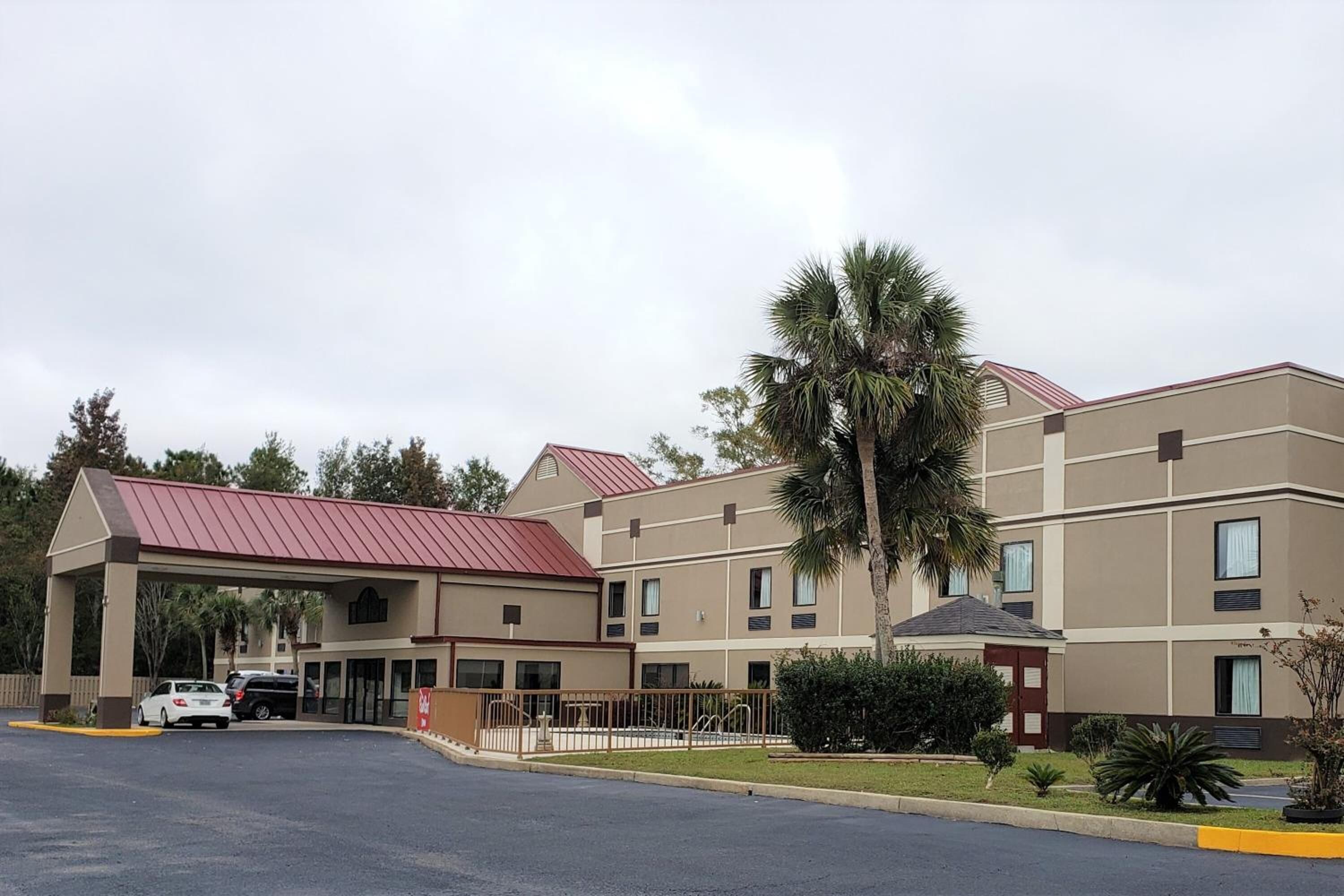 A multi-story hotel with a red roof, a covered parking area, and a palm tree in the foreground.