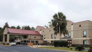A multi-story hotel with a red roof, a covered parking area, and a palm tree in the foreground.
