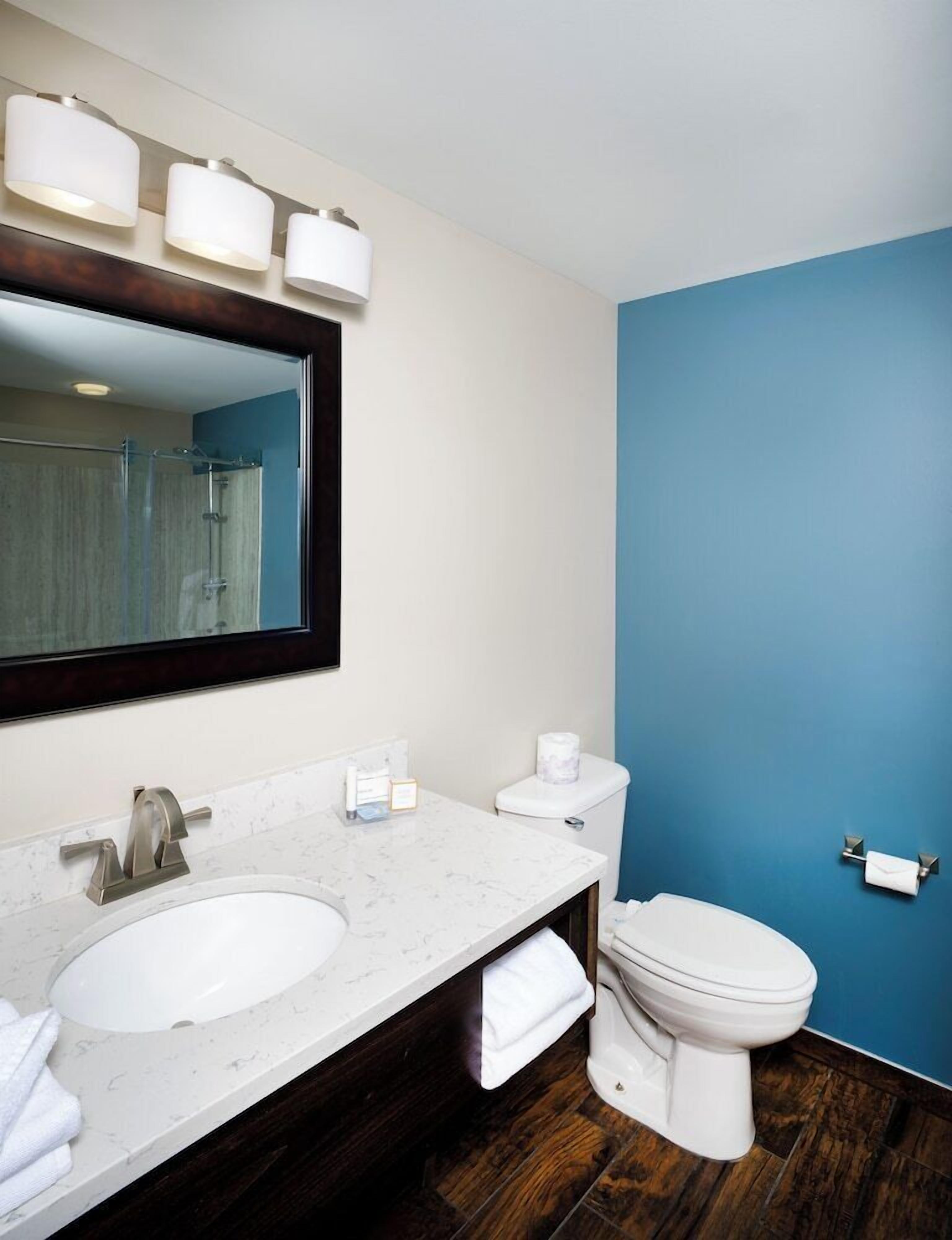 Une salle de bain avec un lavabo blanc, un miroir, des toilettes et un mur bleu.