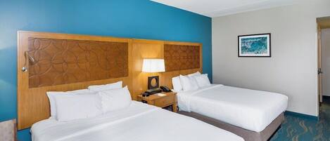 A hotel room with two beds, a wooden headboard, a nightstand with a lamp, and a framed picture on the wall.