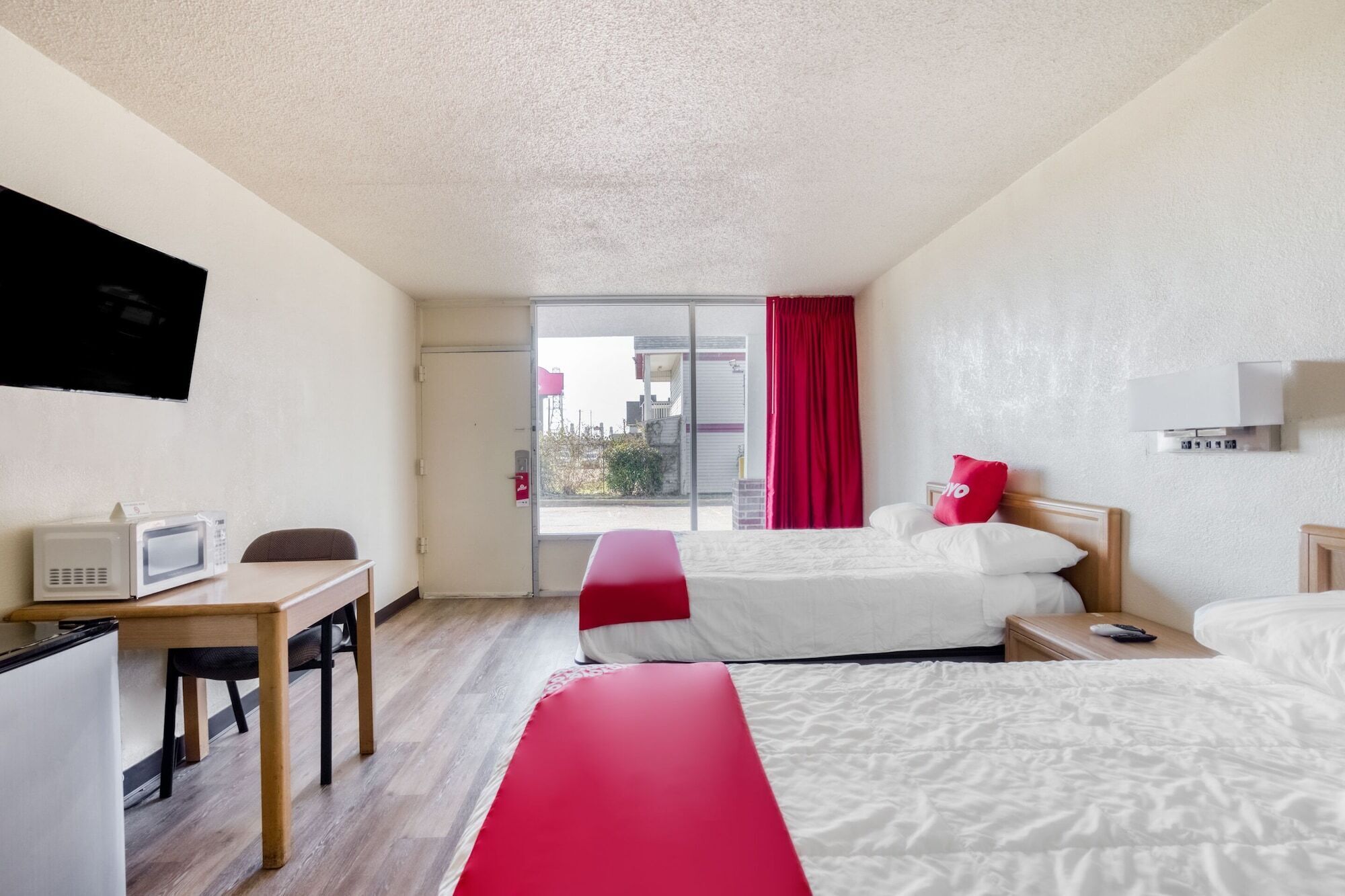 A hotel room with a bed, a desk with a microwave, a TV, and a sliding glass door to the outside.