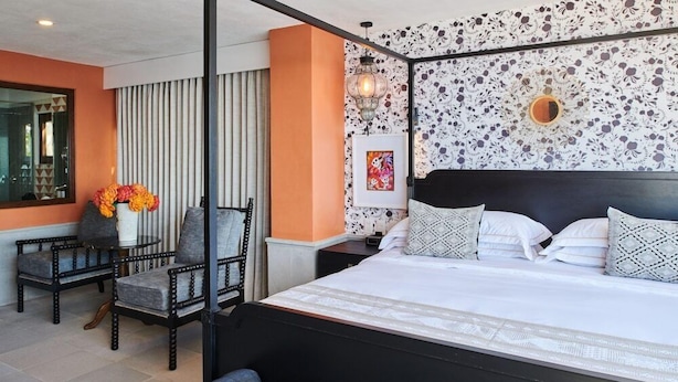 Une chambre d’hôtel avec un grand lit, un bureau avec une chaise, un vase de fleurs et un panneau décoratif au mur.