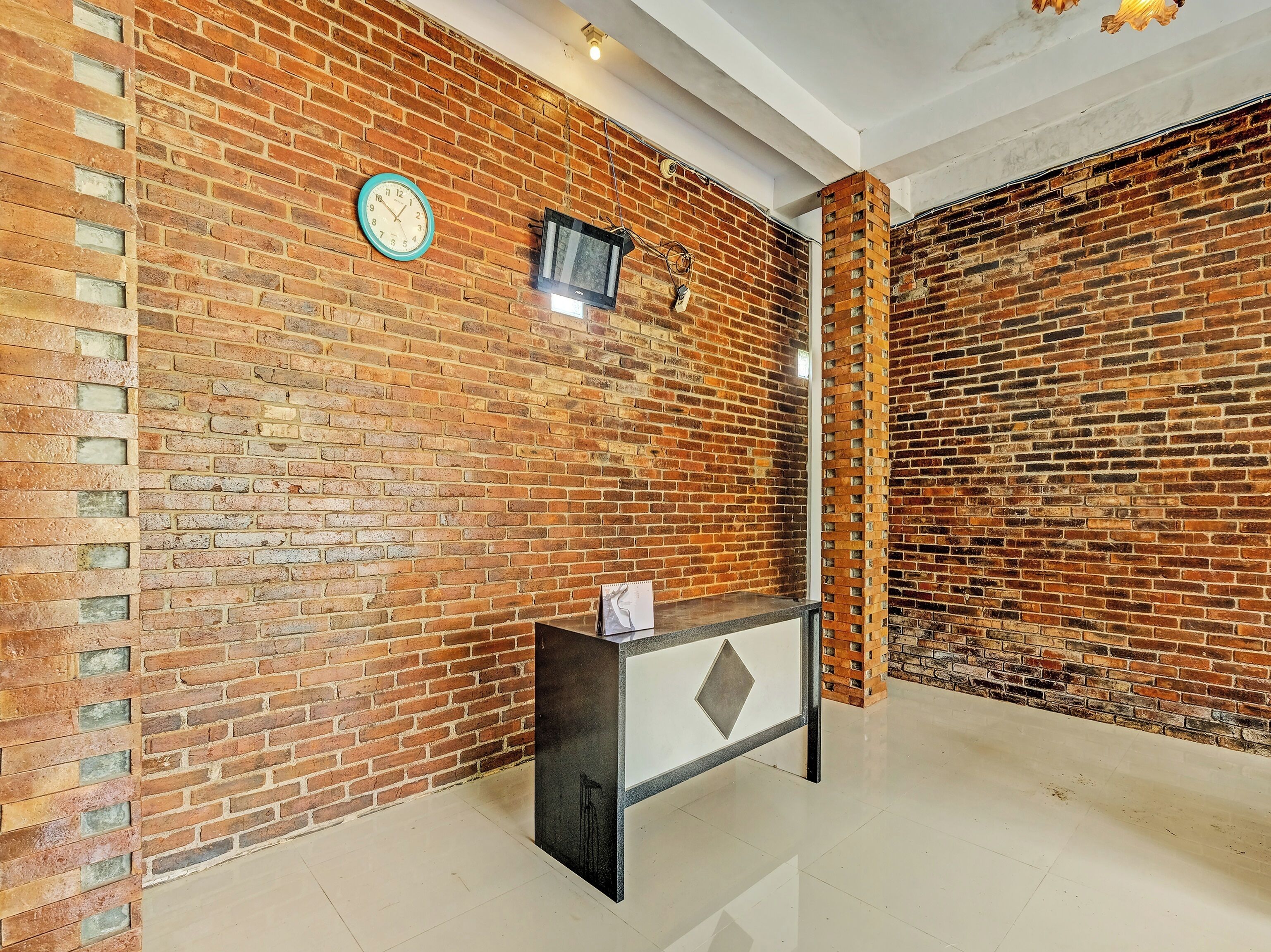 Un vestíbulo con pared de ladrillo, un reloj, un televisor pequeño y un mostrador de recepción.
