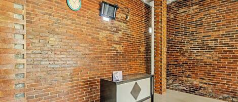 Un vestíbulo con pared de ladrillo, un reloj, un televisor pequeño y un mostrador de recepción.