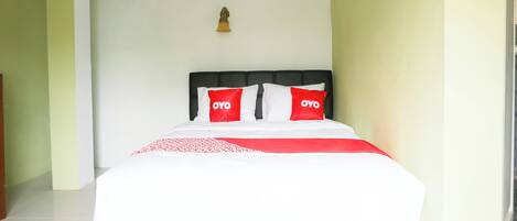 Una cama con ropa blanca y dos almohadas rojas con el texto "OYO", cabecera negra y una lámpara pequeña de pared.