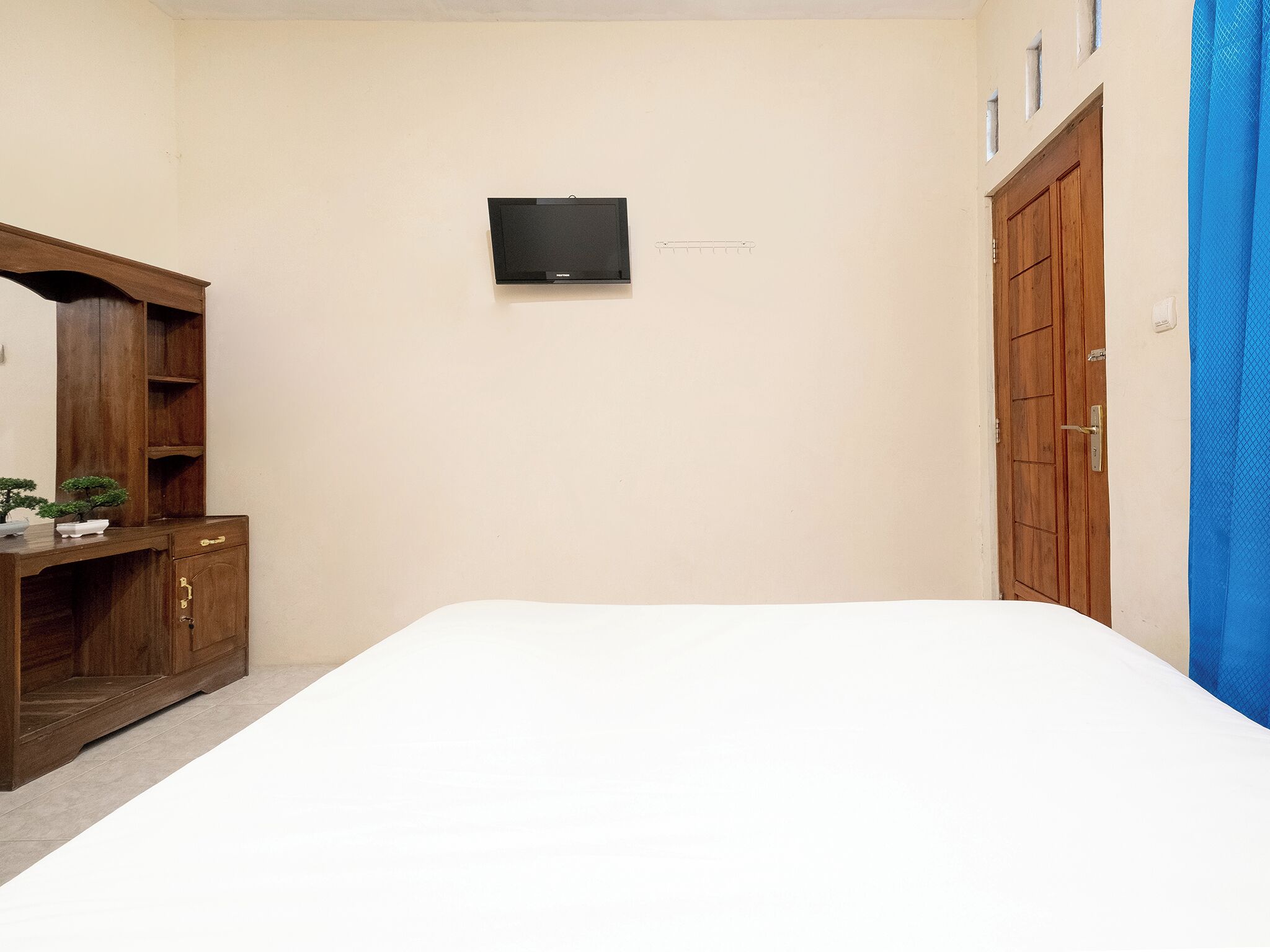 A bedroom with a bed, a wooden dresser, a TV mounted on the wall, and a blue curtain.