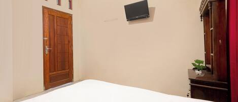 A bedroom with a wooden door, a flat-screen TV mounted on the wall, and a small bedside table with a plant.