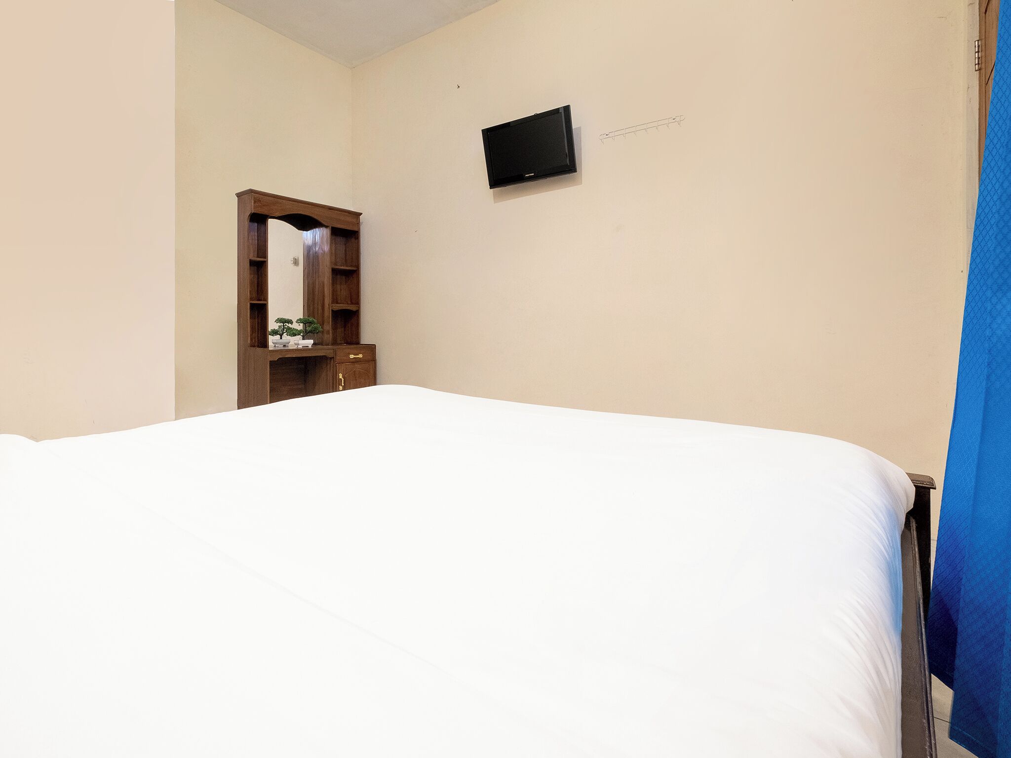 A bedroom with a bed, a wooden dresser, a mirror, and a flat-screen TV mounted on the wall.