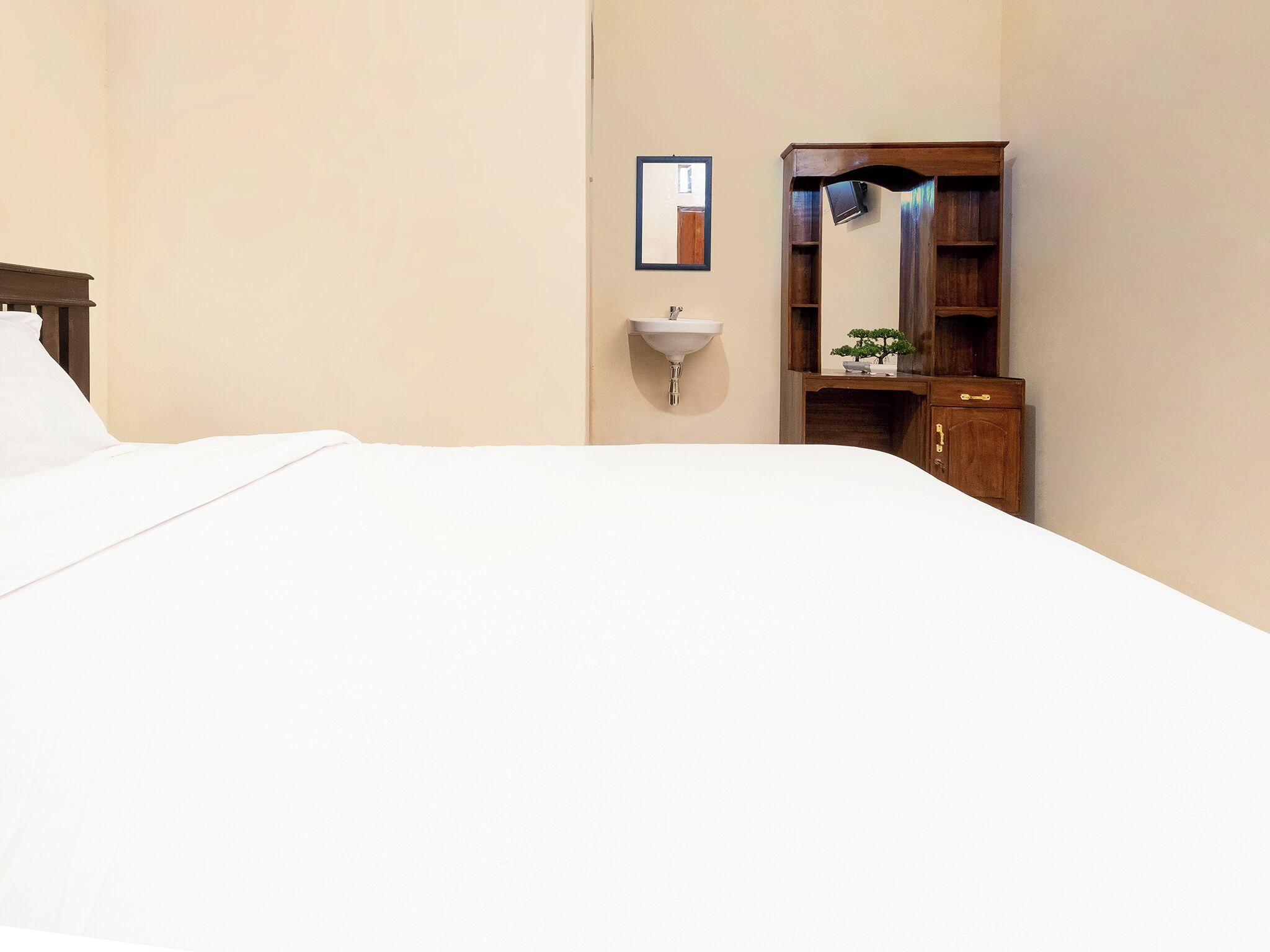 A hotel room with a bed, a wooden wardrobe, a wall-mounted sink, and a framed mirror.