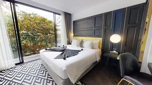 A hotel room with a large bed, a desk, a chair, a window with a view of trees, and a patterned rug.