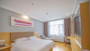Habitación de hotel con una cama grande, un escritorio, una silla y un ventanal con cortinas.
